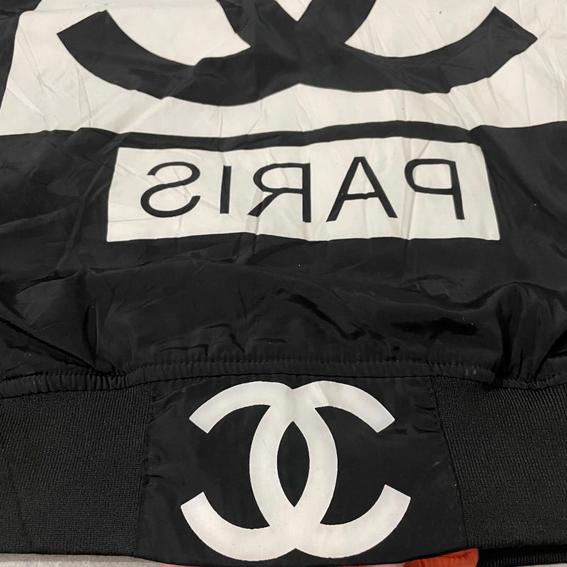May include: Black and white jacket with the word "PARIS" in white block letters. The jacket features a large white logo on the top and bottom. The jacket is made of a shiny material.