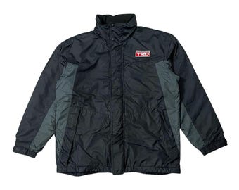 May include: Black and gray jacket with a high collar and a small red and white logo on the chest. The jacket has a full-length zipper and gray panels on the sides. The jacket is made of a lightweight material.