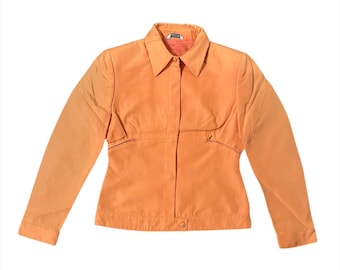 May include: An orange jacket with a collared neckline and long sleeves. The jacket has a button closure and a fitted waist. The fabric appears to be a lightweight material, suitable for layering. The jacket is a solid color with no visible patterns.