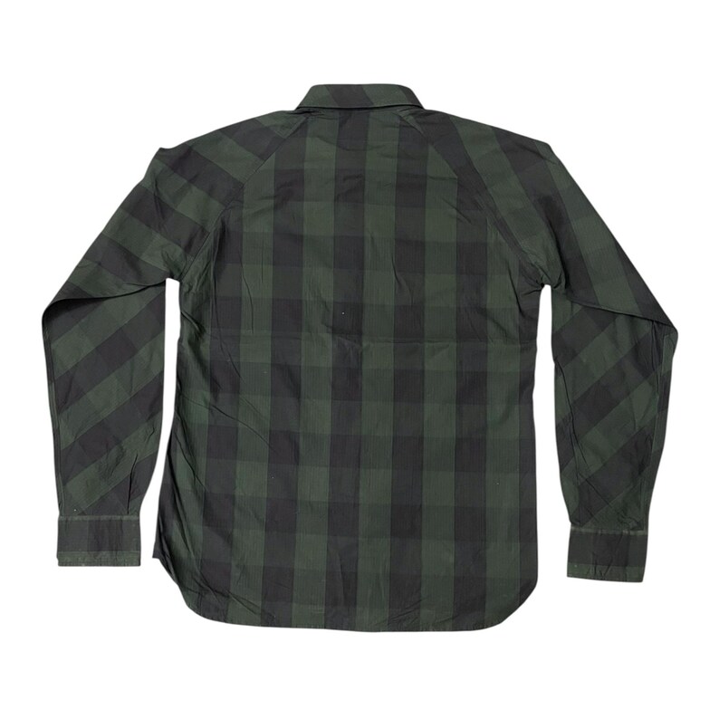 May include: A long-sleeved, button-down shirt in a green and black plaid pattern. The shirt has a classic collar, buttoned cuffs, and a curved hemline. The back of the shirt is visible, showcasing the plaid design.