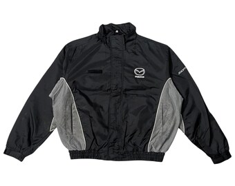 May include: Black and gray Mazda jacket with a white trim. The jacket has a high collar, a zipper closure, and the Mazda logo on the chest. The word "zoom" is printed on the right sleeve.
