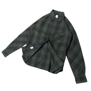 May include: Green and black plaid button-down shirt with long sleeves. The shirt has a chest pocket and a collar. The fabric is a checkered pattern. The shirt is unbuttoned, revealing the interior.