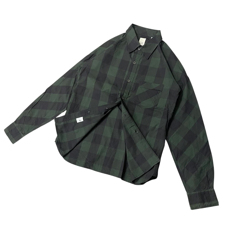 May include: Green and black plaid button-down shirt with long sleeves. The shirt has a chest pocket and a collar. The fabric is a checkered pattern. The shirt is unbuttoned, revealing the interior.