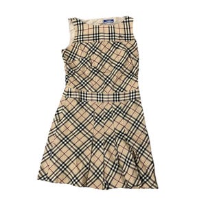 May include: A sleeveless beige dress with a classic plaid pattern in black, red, and white. The dress features a fitted bodice, a defined waist, and a pleated skirt. A small label is visible near the neckline.