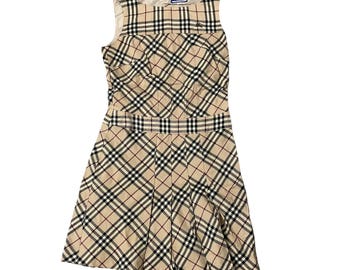 May include: A sleeveless beige dress with a classic plaid pattern in black, red, and white. The dress features a fitted bodice, a defined waist, and a pleated skirt. A small label is visible near the neckline.