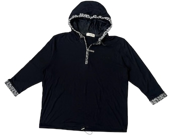 May include: A black hooded sweatshirt with long sleeves. The hood and sleeve cuffs feature a white and black patterned trim. The sweatshirt has a quarter-zip closure and a drawstring at the waist. The brand name is visible on the label.