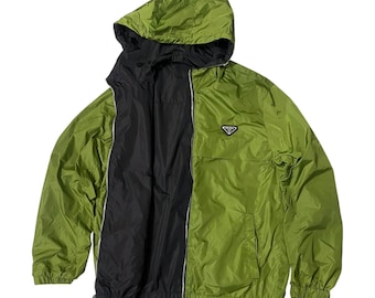 May include: A reversible hooded jacket in green and black. The jacket has a full zipper, a small logo on the chest, and a hood. The jacket is made of a lightweight material, and the interior is black.
