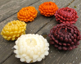 May include: Assortment of six colorful wax candles shaped like chrysanthemums. The candles are in shades of yellow, orange, white, and burgundy.