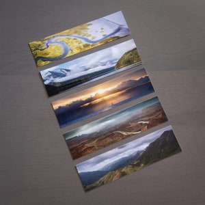 May include: Five different landscape photographs printed on rectangular cards. The cards feature a variety of scenes, including a river delta, a mountain range, a lake, a sunset, and a desert canyon.