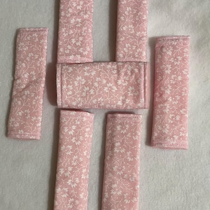 May include: Seven pink fabric straps with a white floral pattern. The straps are all the same size and are arranged in a staggered pattern.