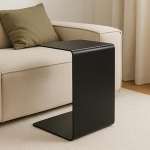 Può includere: Un tavolino da salotto in metallo nero con un design curvo. Il tavolino è accanto a un divano bianco con un cuscino verde.