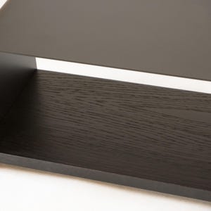 May include: A contemporary coffee table with a dark, matte finish. The table has a rectangular shape with a solid, dark wood grain shelf and a sleek, curved metal top. The design is minimalist and modern, suitable for a living room.