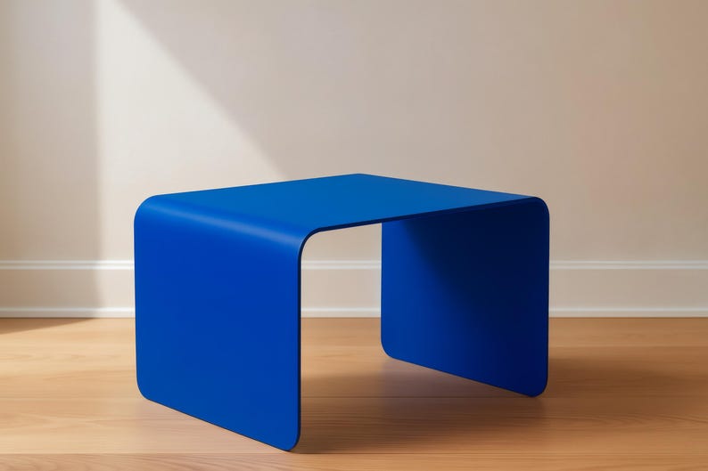 An ultramarine blue curved metal side table sitting on a light wood floor next to a white wall.