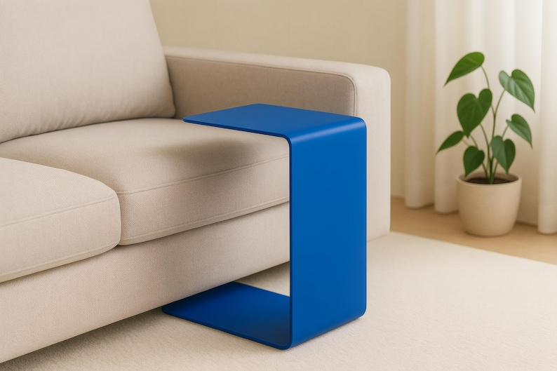 A blue C-shaped metal side table is placed with its base under a light beige sofa, extending over the seat.