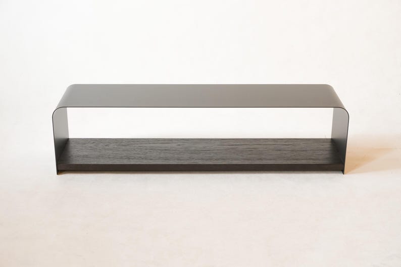 May include: A contemporary coffee table featuring a dark grey metal frame and a dark wood shelf. The table has a rectangular form with rounded corners and measures approximately 122 cm long, 30 cm wide, and 36 cm high.