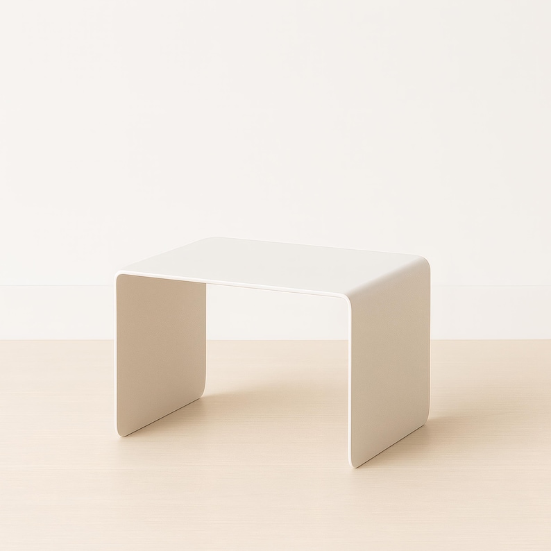 A white minimalist bent metal side table resting on a light wood floor against a white wall.