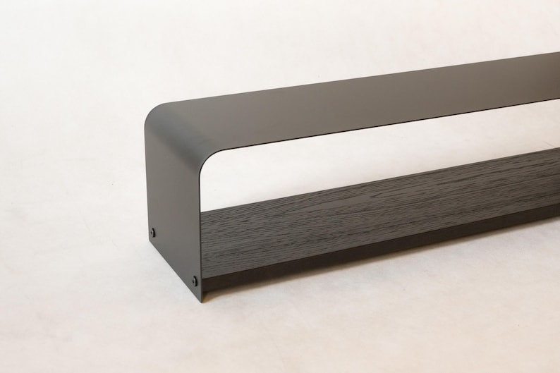 May include: A contemporary, dark grey metal shelf with a curved top and a dark wood base. The shelf is rectangular with a hollow centre, and is designed for displaying items. The minimalist design is suitable for various home decor styles.