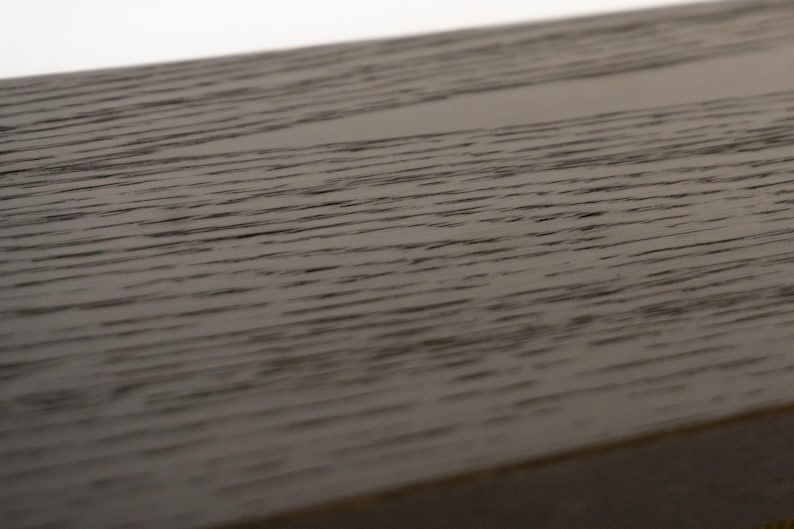 May include: Close-up of a section of dark brown wood with a visible grain pattern. The wood appears to be part of a larger structure, possibly a table or a piece of furniture. The surface is smooth and has a slight sheen.