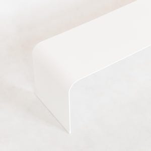 May include: A minimalist, white, modern-style table or shelf with a rounded corner. The object is set against a white background, creating a clean and simple aesthetic. The design is sleek and contemporary.