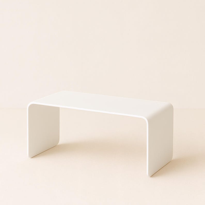 A white minimalist metal coffee table with rounded edges on a pale surface against a neutral background.