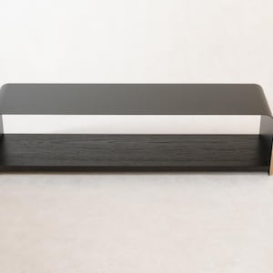May include: A contemporary black shelf with a curved top and a wooden base. The shelf is made of metal and wood. It is designed to be mounted on a wall or placed on a surface. The shelf is approximately 60 cm long.