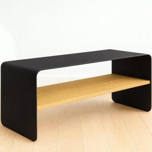 A black metal bench with rounded corners and a light wood shelf, shown at an angle on a light wood floor against a white wall.