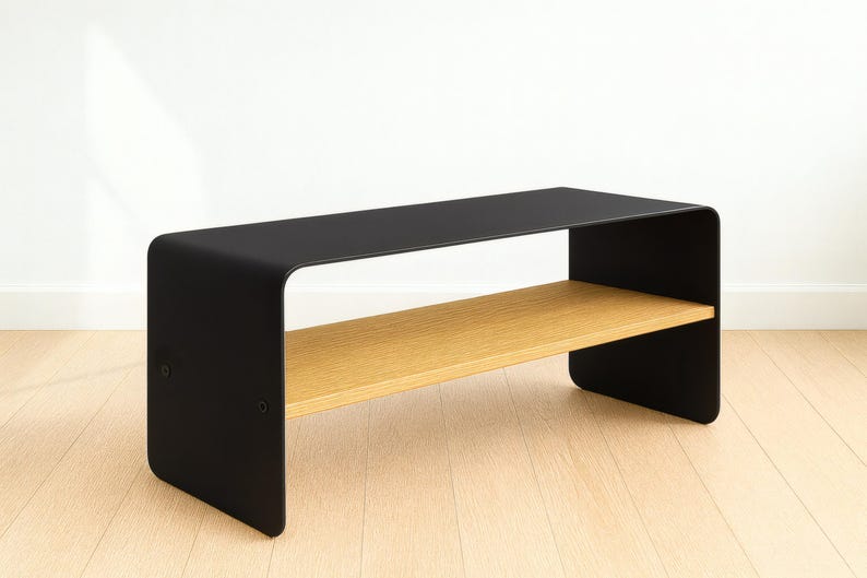 A black metal bench with rounded corners and a light wood shelf, shown at an angle on a light wood floor against a white wall.