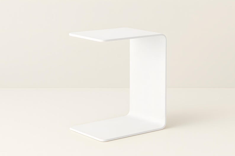 A white C-shaped metal side table is shown from a slight angle against a light beige background.