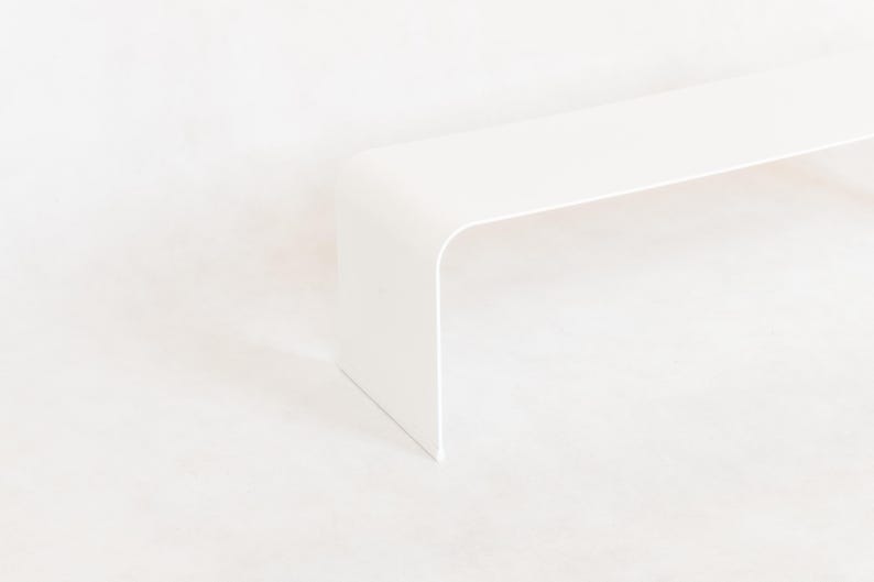 May include: A minimalist, white, modern bench with a curved design. The bench has a rectangular top and a single, curved leg. The bench is made of a solid, opaque material and is set against a white background.