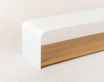 May include: A modern, rectangular shelf with a white, curved top and a natural wood base. The shelf is designed with clean lines and a minimalist aesthetic, suitable for home decor.