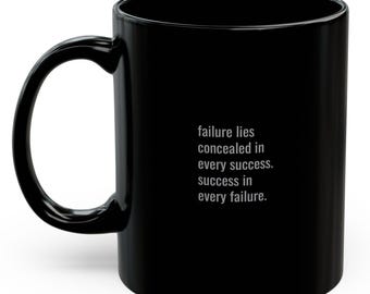 Puede incluir: Taza de café de cerámica negra con una cita inspiradora blanca que dice: "El fracaso se esconde en cada éxito. El éxito en cada fracaso."