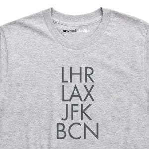 Könnte beinhalten: Graues T-Shirt mit den Flughafencodes LHR, LAX, JFK und BCN in Schwarz gedruckt.