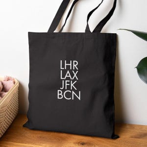 May include: Black canvas tote bag with white text that reads "LHR LAX JFK BCN".