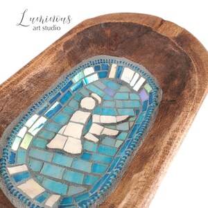 May include: A wooden bowl featuring a blue and white mosaic design of a person. The mosaic is set into the wood and has a blue border.