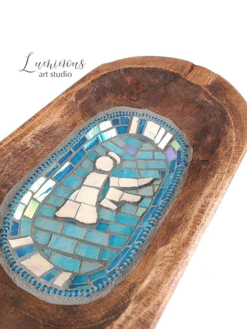 May include: A wooden bowl featuring a blue and white mosaic design of a person. The mosaic is set into the wood and has a blue border.