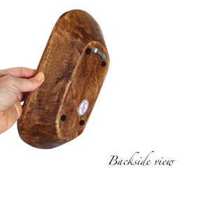 May include: A wooden bowl with a dark brown stain. The bowl has a rounded oval shape and is shown from the bottom. The bowl has three small black dots on the bottom and a small silver metal hook.