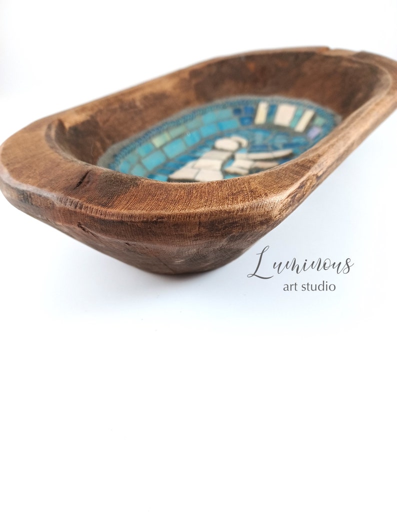 May include: A wooden dough bowl with a blue and white mosaic design featuring a stylised angel figure. The bowl is made of natural wood and has a rustic, handcrafted look.