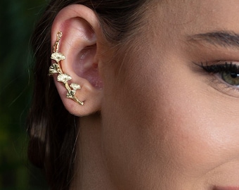 May include: A woman with long brown hair wearing a gold chain necklace and gold jewelry in her ear and lip. The jewelry features a delicate butterfly design.