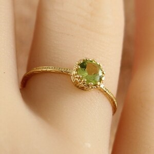 May include: A delicate gold ring with a green gemstone set in a crown-like design.