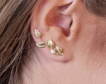 May include: Gold leaf ear cuff with a small pearl accent. The ear cuff is designed to wrap around the ear and features a delicate, leafy design.