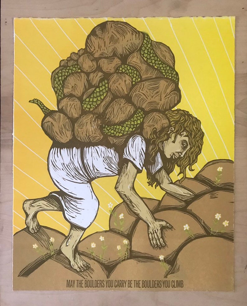 May include: A woodcut print of a person carrying a large pile of rocks on their back, climbing up a rocky hill. The print is in shades of brown, green, and yellow. The text at the bottom reads "May the boulders you carry be the boulders you climb."