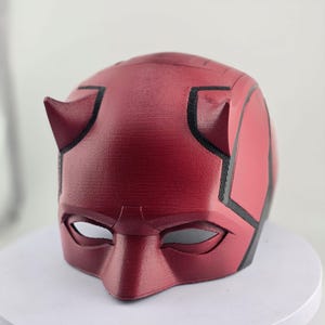 Op de afbeelding: Een rood en zwart 3D-geprint Daredevil-masker met hoorns en oogopeningen.