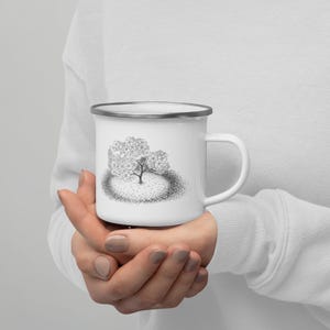Puede incluir: Taza de esmalte blanco con una ilustración en blanco y negro de un árbol con un tronco y ramas gruesas. El árbol está rodeado por un círculo de pequeños puntos.