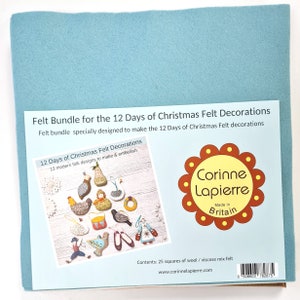 Könnte beinhalten: Ein hellblaues Filzbündel für die 12 Tage der Weihnachts-Filzdekorationen. Das Paket enthält 25 Quadrate aus Wolle/Viskose-Mix-Filz. Das Paket zeigt eine Vielzahl von Filzdekorationen, darunter eine Birne, ein Huhn und ein Vogel.