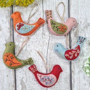 May include: Five felt bird ornaments with embroidered details. The birds are in shades of orange, pink, green, blue, and red. Each bird has a loop for hanging.