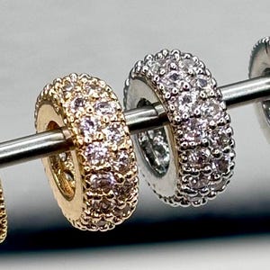 May include: Three charm beads with a pave setting of clear cubic zirconia stones. The beads are in gold, silver, and rose gold.