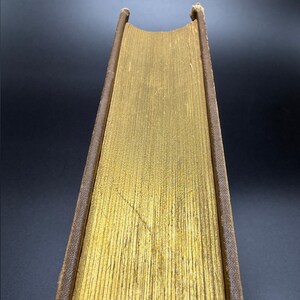 May include: The spine of a vintage book with a gold-colored cover and brown leather binding.