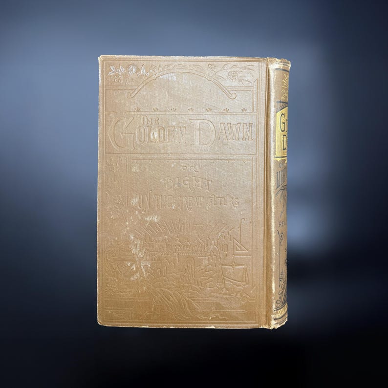May include: The cover of a vintage book titled "The Golden Dawn" with the subtitle "The Light Until the Great Time". The cover is brown with a decorative design of a ship and a landscape.