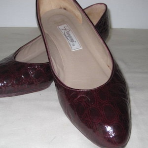 May include: A pair of burgundy leather flats with a crocodile embossed pattern. The shoes have a pointed toe and a low heel. The brand name "Donnari" is visible on the insole.