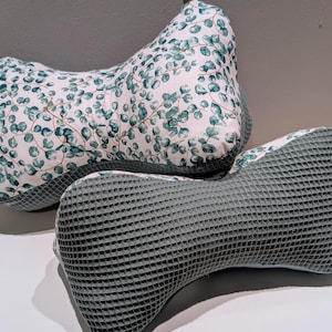 Może przedstawiać: Dwa poduszki, jedna z białym tłem i zielonym wzorem liści, a druga z szarą fakturą wafelkową.